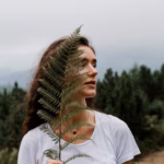 girl-holding-leaf-fern-travelling-mountains-foggy-day_255847-1947